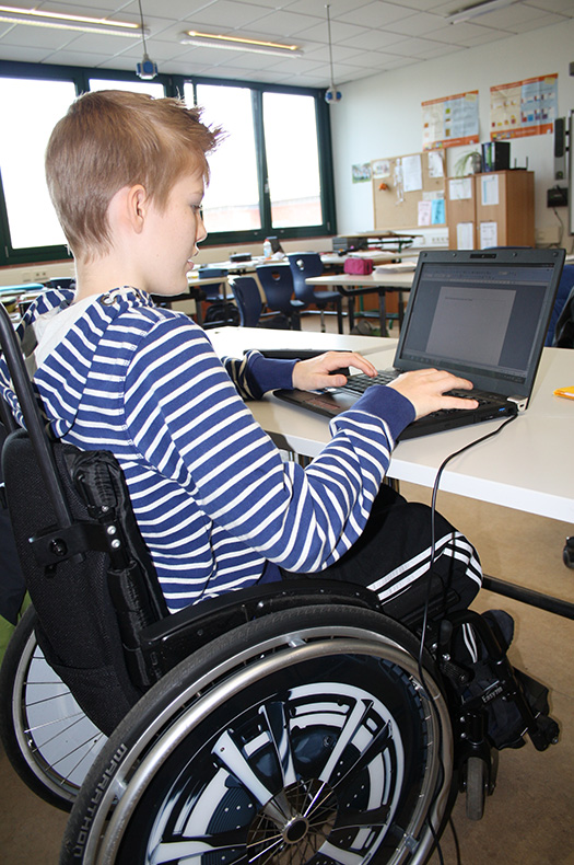 Foto: Ein Jugendlicher im Rollstuhl arbeitet am Laptop im Klassenraum